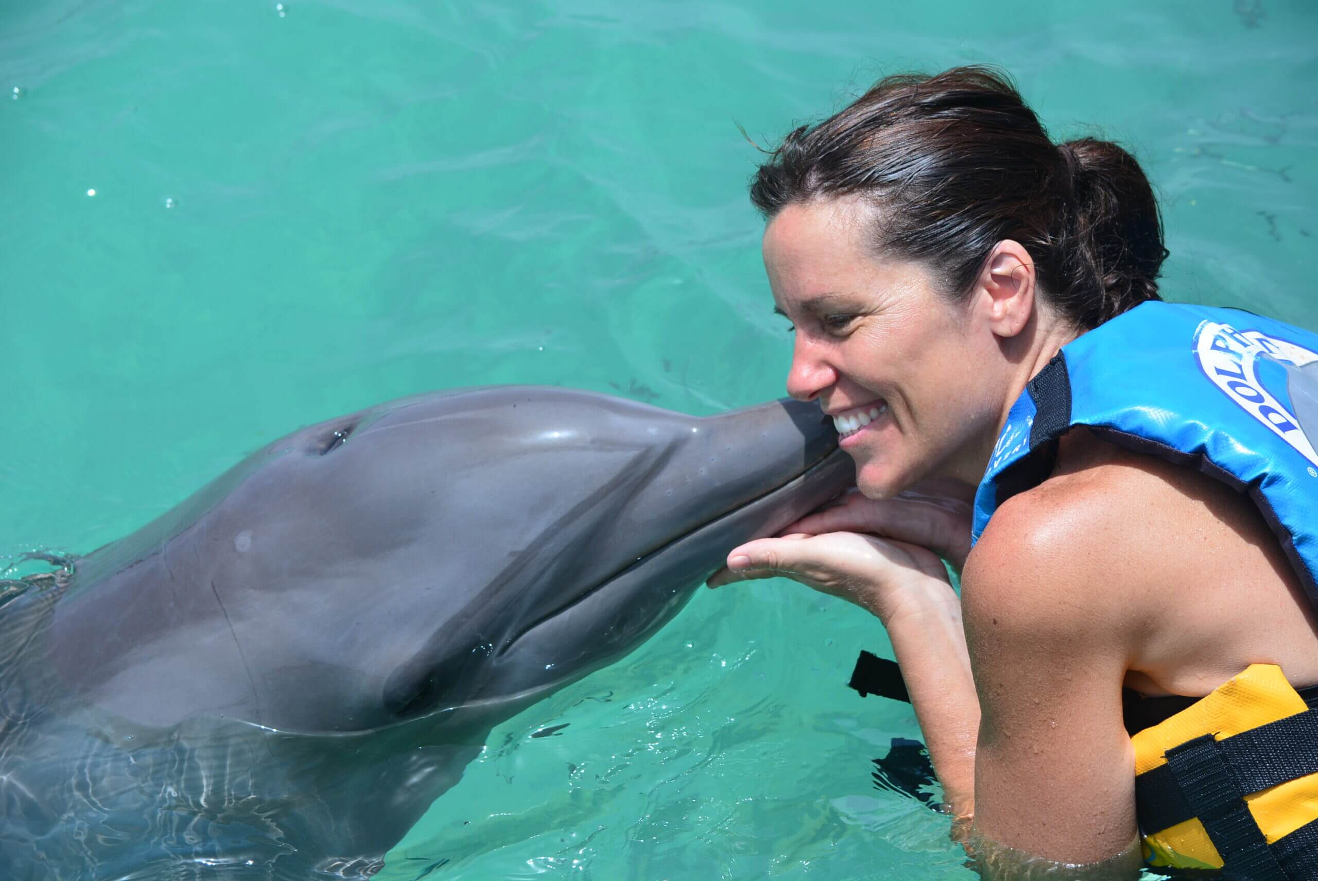 Woman smiling while dolphin kisses her cheek.